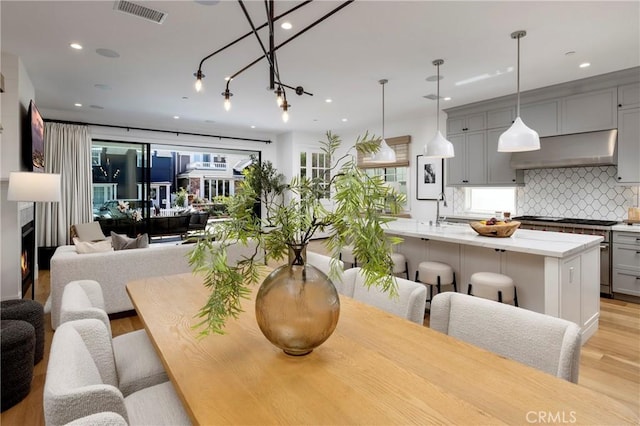 dining room featuring light wood-type flooring, visible vents, a premium fireplace, and recessed lighting