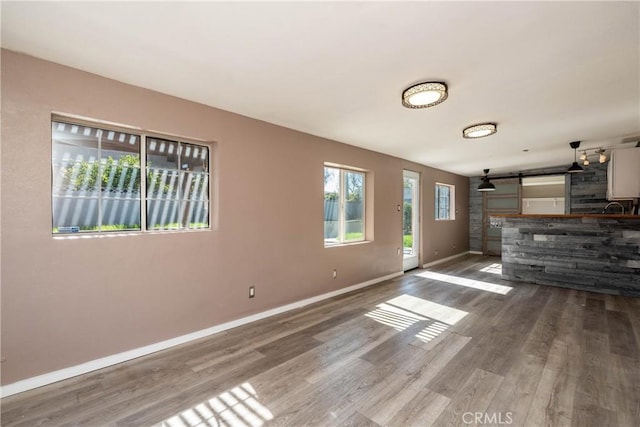 unfurnished living room featuring baseboards, a barn door, and wood finished floors