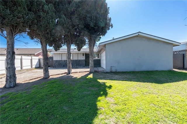 rear view of house with a yard, fence, and stucco siding