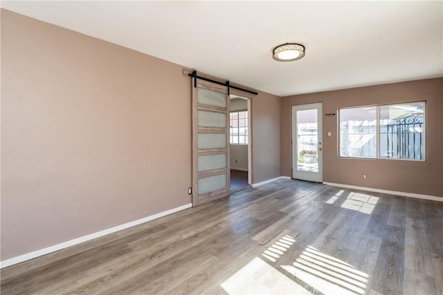 unfurnished room with a barn door, baseboards, and wood finished floors