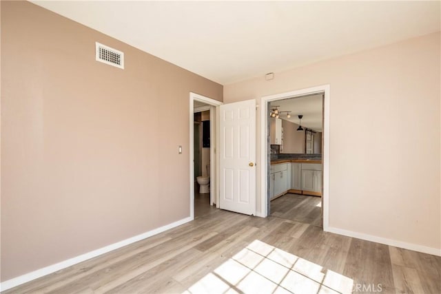 unfurnished bedroom featuring connected bathroom, baseboards, visible vents, and light wood-type flooring