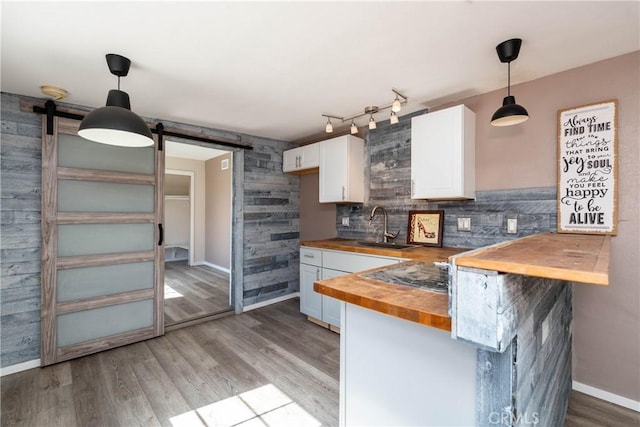 kitchen featuring light wood finished floors, a sink, white cabinets, wood counters, and a barn door