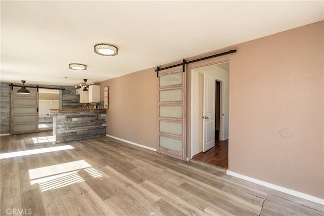 unfurnished living room featuring a barn door, baseboards, and light wood finished floors