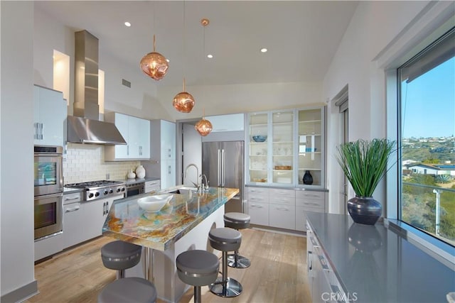 kitchen featuring a sink, light wood-style floors, appliances with stainless steel finishes, a breakfast bar area, and wall chimney range hood