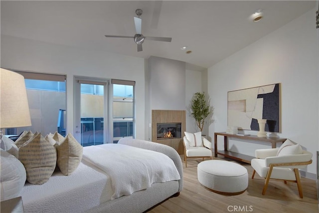 bedroom featuring a tiled fireplace, access to exterior, wood finished floors, ceiling fan, and vaulted ceiling