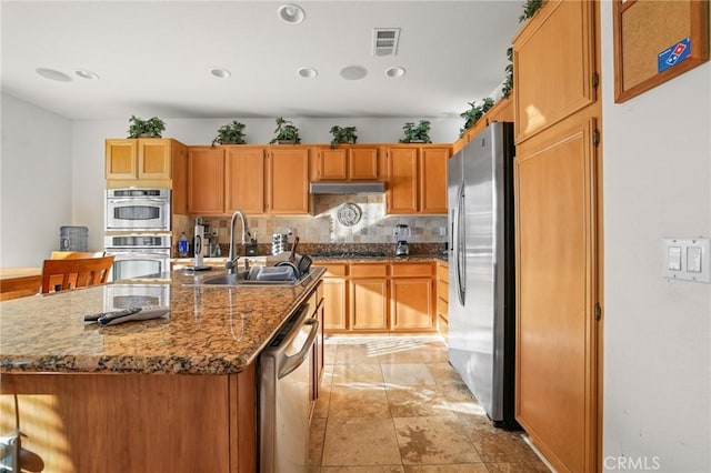 kitchen featuring visible vents, a center island with sink, a sink, appliances with stainless steel finishes, and decorative backsplash