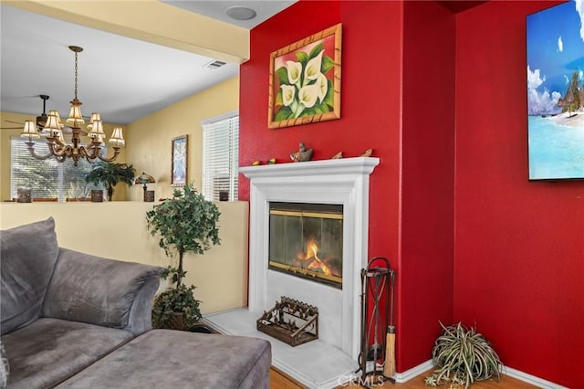 living room featuring visible vents, wood finished floors, a glass covered fireplace, baseboards, and a chandelier