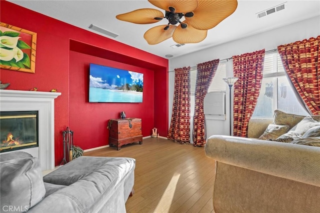 living room featuring visible vents, ceiling fan, a glass covered fireplace, and hardwood / wood-style floors