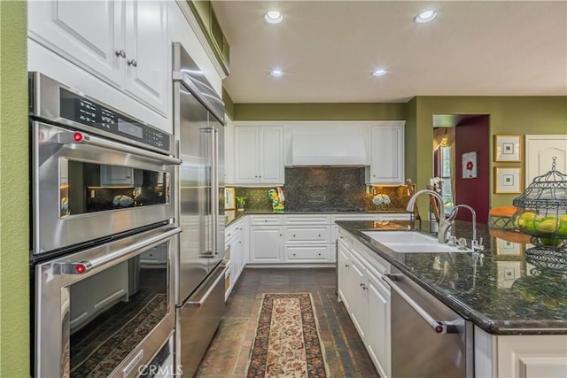 kitchen featuring custom range hood, white cabinetry, backsplash, appliances with stainless steel finishes, and a sink