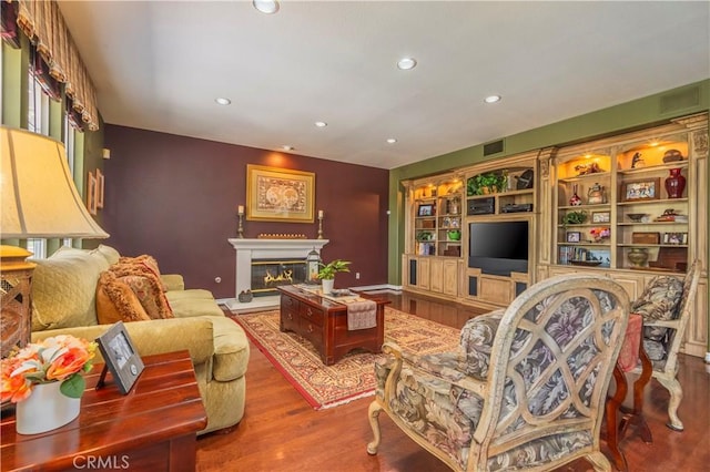 living room with wood finished floors, a glass covered fireplace, visible vents, and recessed lighting