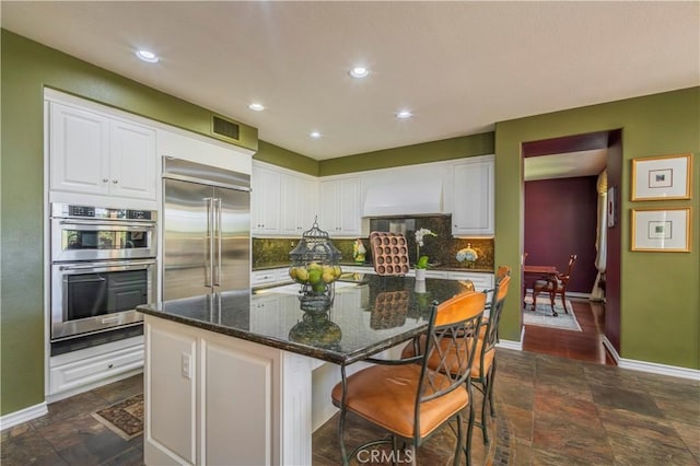 kitchen with tasteful backsplash, stone finish flooring, visible vents, white cabinets, and stainless steel appliances