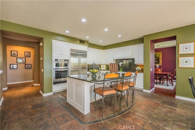 kitchen featuring appliances with stainless steel finishes, stone finish floor, baseboards, and white cabinetry