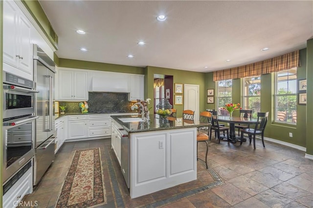kitchen featuring tasteful backsplash, baseboards, a sink, recessed lighting, and stone tile floors