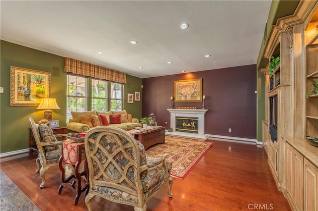 living area with recessed lighting, baseboards, wood finished floors, and a glass covered fireplace
