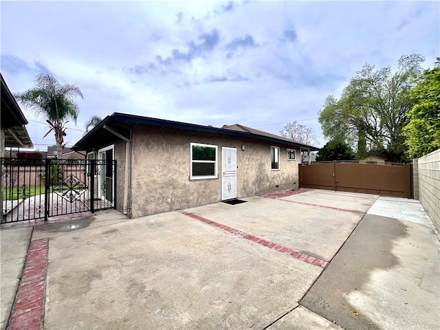 back of house featuring stucco siding, fence, a patio, and a gate