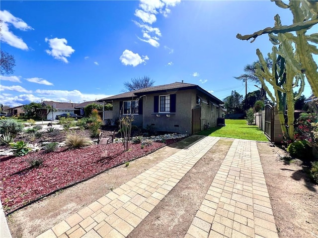 view of front of house featuring stucco siding, driveway, a front lawn, fence, and crawl space