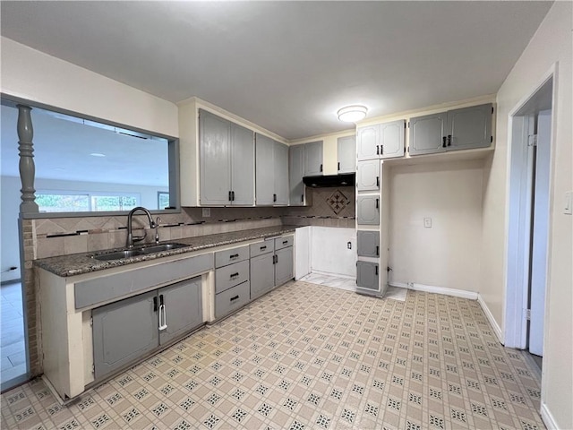 kitchen featuring tasteful backsplash, gray cabinetry, under cabinet range hood, light floors, and a sink