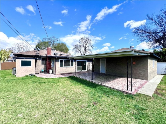 rear view of house with a yard, a patio area, a chimney, and stucco siding