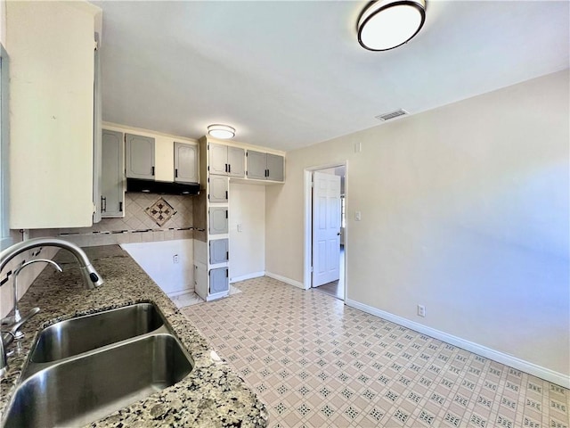 kitchen with light stone countertops, baseboards, visible vents, a sink, and tasteful backsplash