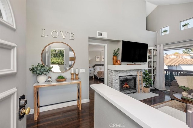 living room with visible vents, baseboards, a lit fireplace, high vaulted ceiling, and dark wood-style flooring