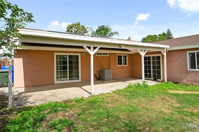 back of property with central air condition unit, a patio area, a lawn, and stucco siding