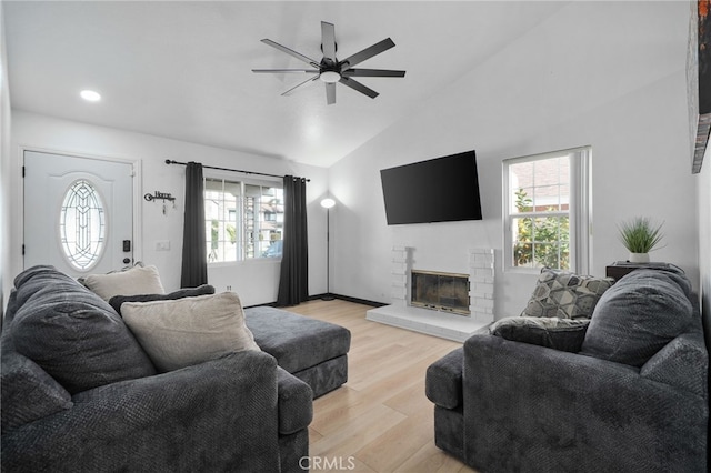 living room with a wealth of natural light, a glass covered fireplace, light wood-style floors, and vaulted ceiling