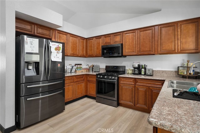 kitchen with light wood-type flooring, vaulted ceiling, appliances with stainless steel finishes, brown cabinetry, and a sink