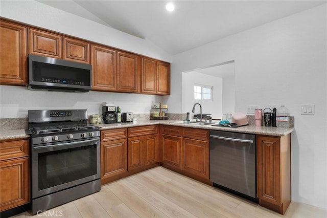 kitchen with a sink, stainless steel appliances, lofted ceiling, and brown cabinets