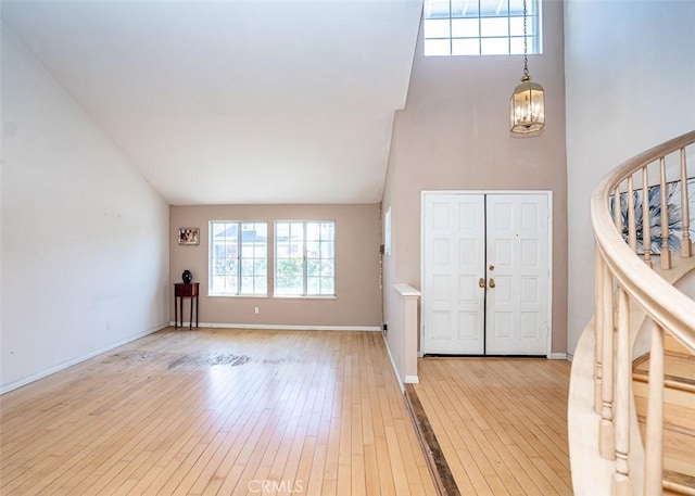 foyer entrance featuring hardwood / wood-style floors, an inviting chandelier, baseboards, and high vaulted ceiling