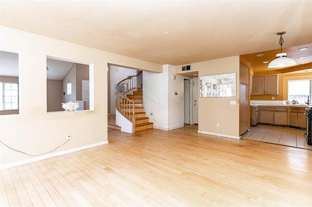 unfurnished living room with light wood-type flooring, visible vents, a wealth of natural light, and stairway