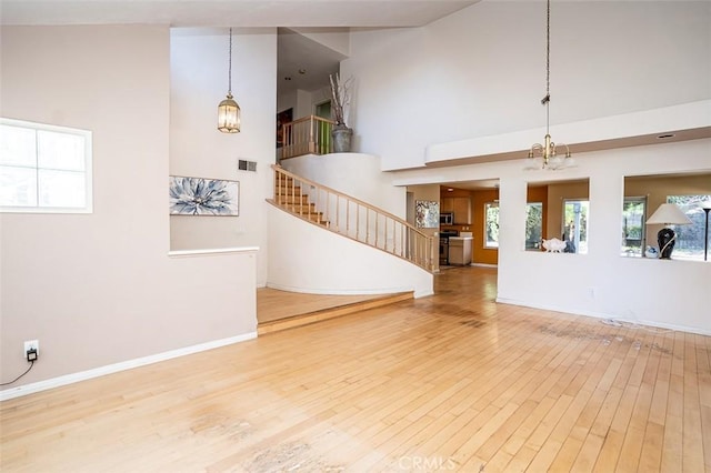 unfurnished living room with visible vents, baseboards, stairs, a high ceiling, and wood finished floors