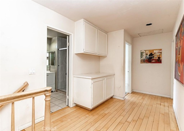 kitchen featuring baseboards, washer / dryer, light countertops, white cabinetry, and light wood-type flooring