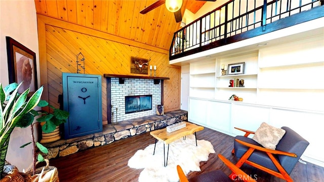 living area with wooden walls, a ceiling fan, wood finished floors, wooden ceiling, and a brick fireplace