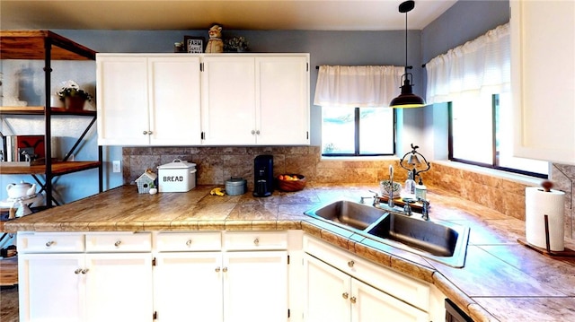 kitchen with a sink, decorative light fixtures, tile countertops, and white cabinetry