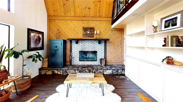 living room with a high ceiling, a brick fireplace, dark wood-style floors, and wood walls