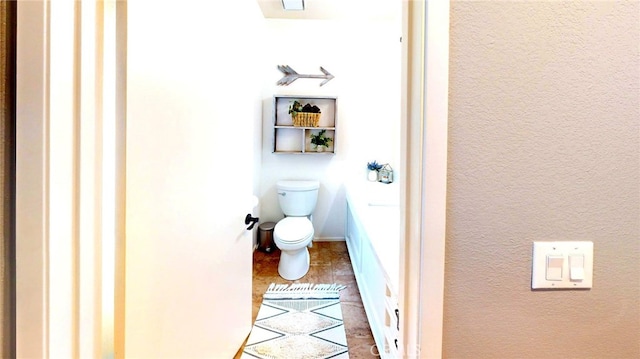 bathroom featuring toilet, a textured wall, and baseboards