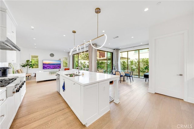 kitchen with light wood finished floors, open floor plan, stainless steel gas stovetop, white cabinetry, and a sink