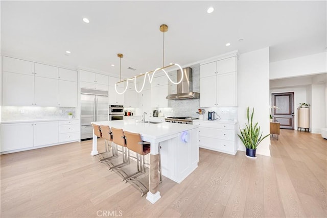 kitchen featuring a breakfast bar, a sink, stainless steel appliances, light countertops, and wall chimney exhaust hood