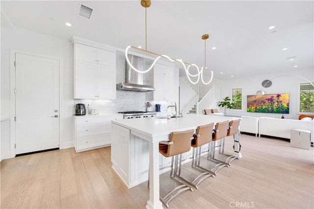 kitchen featuring visible vents, light wood finished floors, a sink, white cabinets, and wall chimney exhaust hood