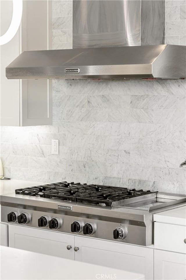 details with decorative backsplash, stainless steel gas stovetop, range hood, and white cabinetry