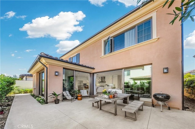 rear view of house with stucco siding, a patio, and outdoor dining space