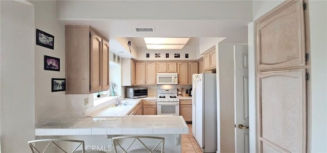 kitchen featuring visible vents, tile counters, a peninsula, white appliances, and a sink