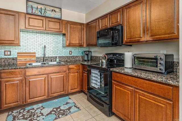 kitchen featuring light tile patterned floors, dark stone counters, a sink, black appliances, and brown cabinets