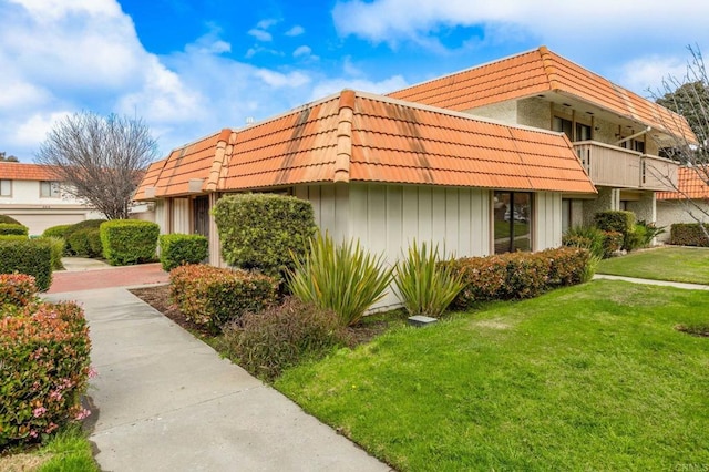 view of home's exterior featuring mansard roof, a tile roof, and a yard