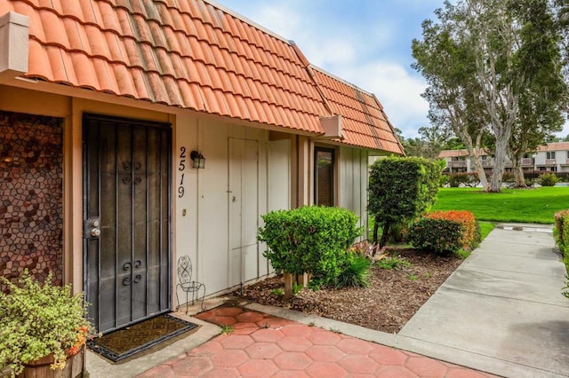 doorway to property with a lawn and a tile roof