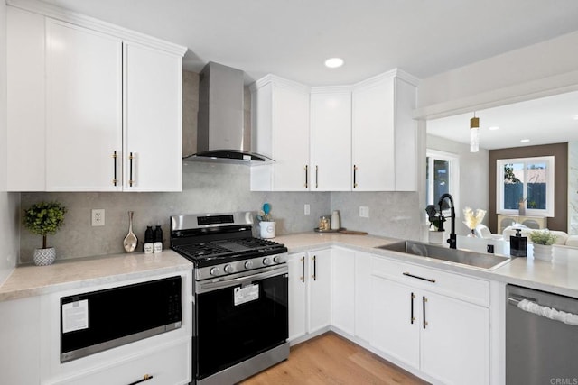 kitchen with stainless steel appliances, wall chimney exhaust hood, light countertops, and a sink