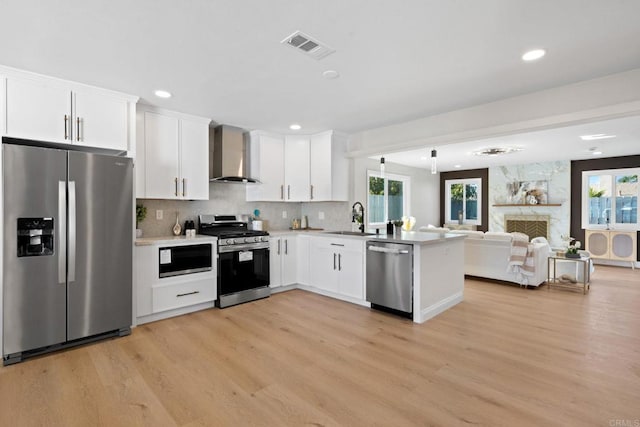 kitchen with visible vents, a sink, stainless steel appliances, a stone fireplace, and wall chimney range hood