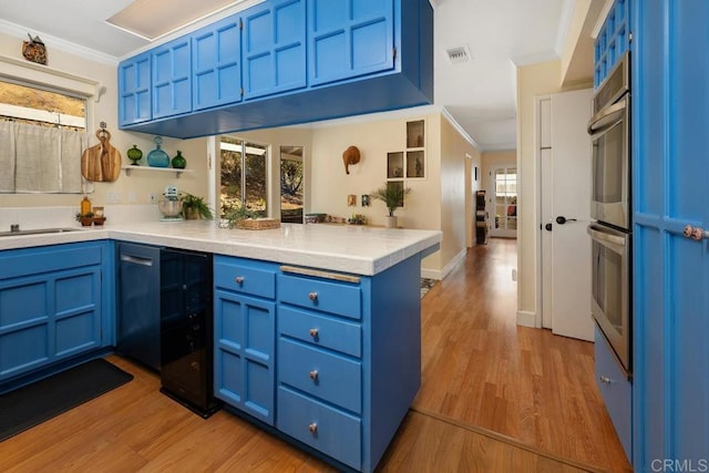 kitchen featuring light wood finished floors, visible vents, blue cabinetry, crown molding, and a peninsula