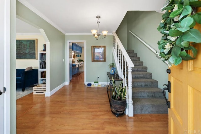 foyer entrance with stairs, ornamental molding, wood finished floors, arched walkways, and a notable chandelier