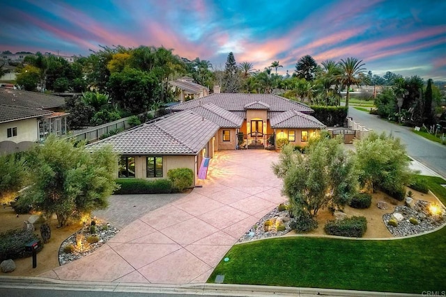 view of front of property with a front lawn, fence, a tile roof, stucco siding, and driveway